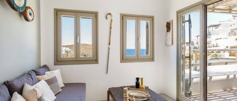 A room with a sofa, a wooden table, and two windows with a view of the sea.