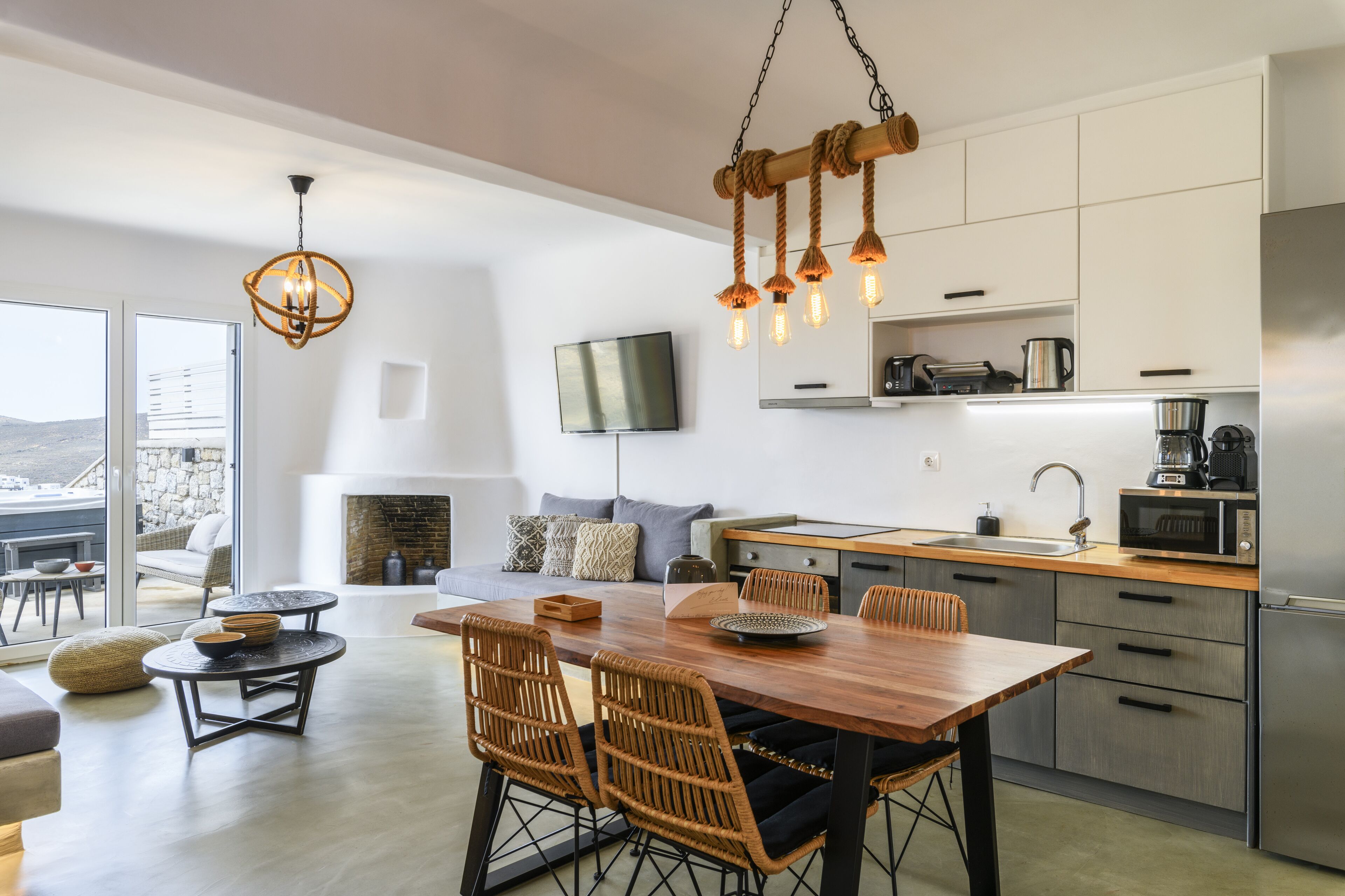 Cozinha moderna com área de refeições, apresentando uma mesa de madeira, cadeiras de vime e um lustre.