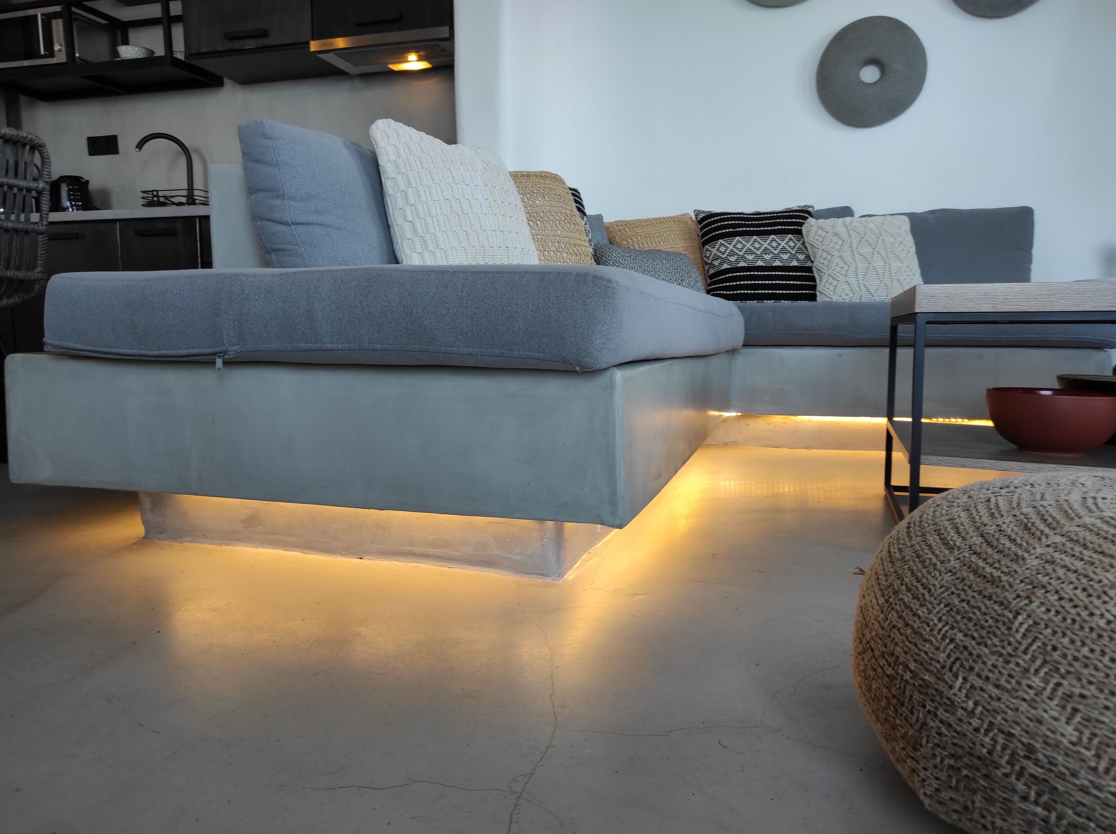 Uma sala de estar moderna com um sofá modular cinza, uma mesinha e um banquinho redondo.