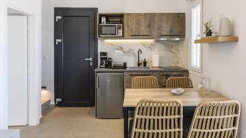 A compact kitchen with a microwave, coffee maker, and a small refrigerator. There is a dining area with wicker chairs and a wooden table.