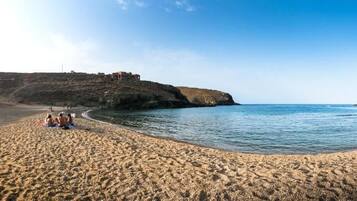 Una playa con gente sentada sobre la arena, un acantilado con edificios y un cielo despejado.