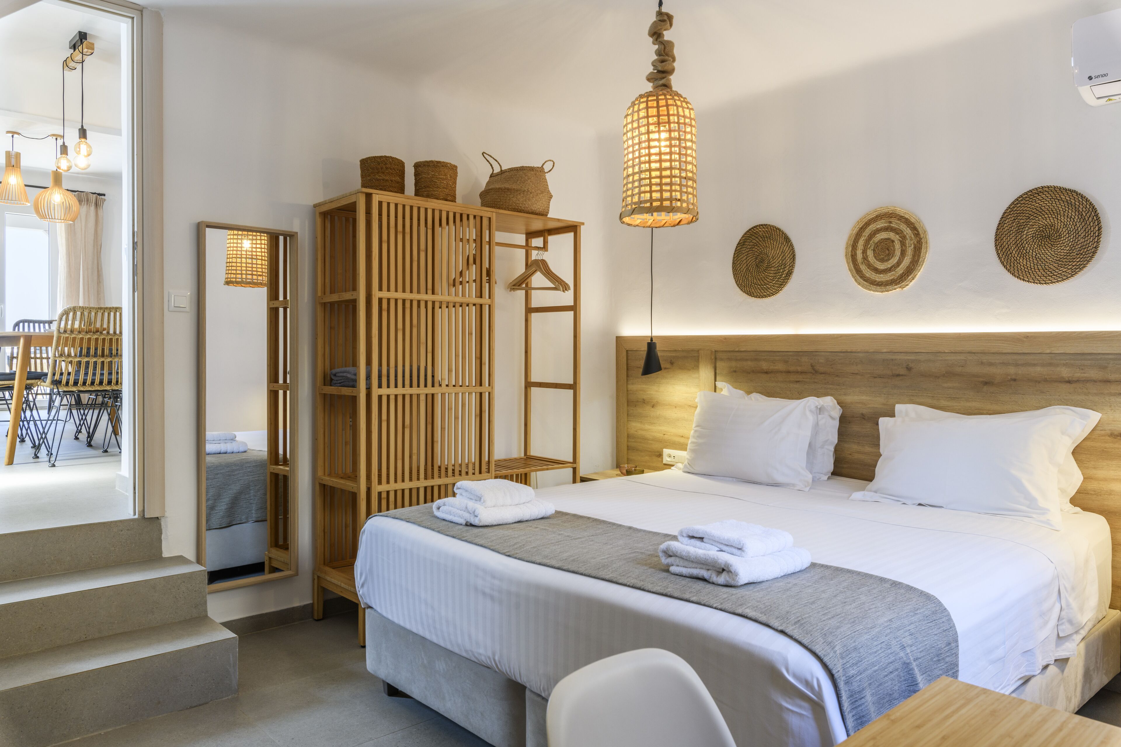 A neatly arranged hotel room with a large bed, a wooden wardrobe, and a hanging light fixture.