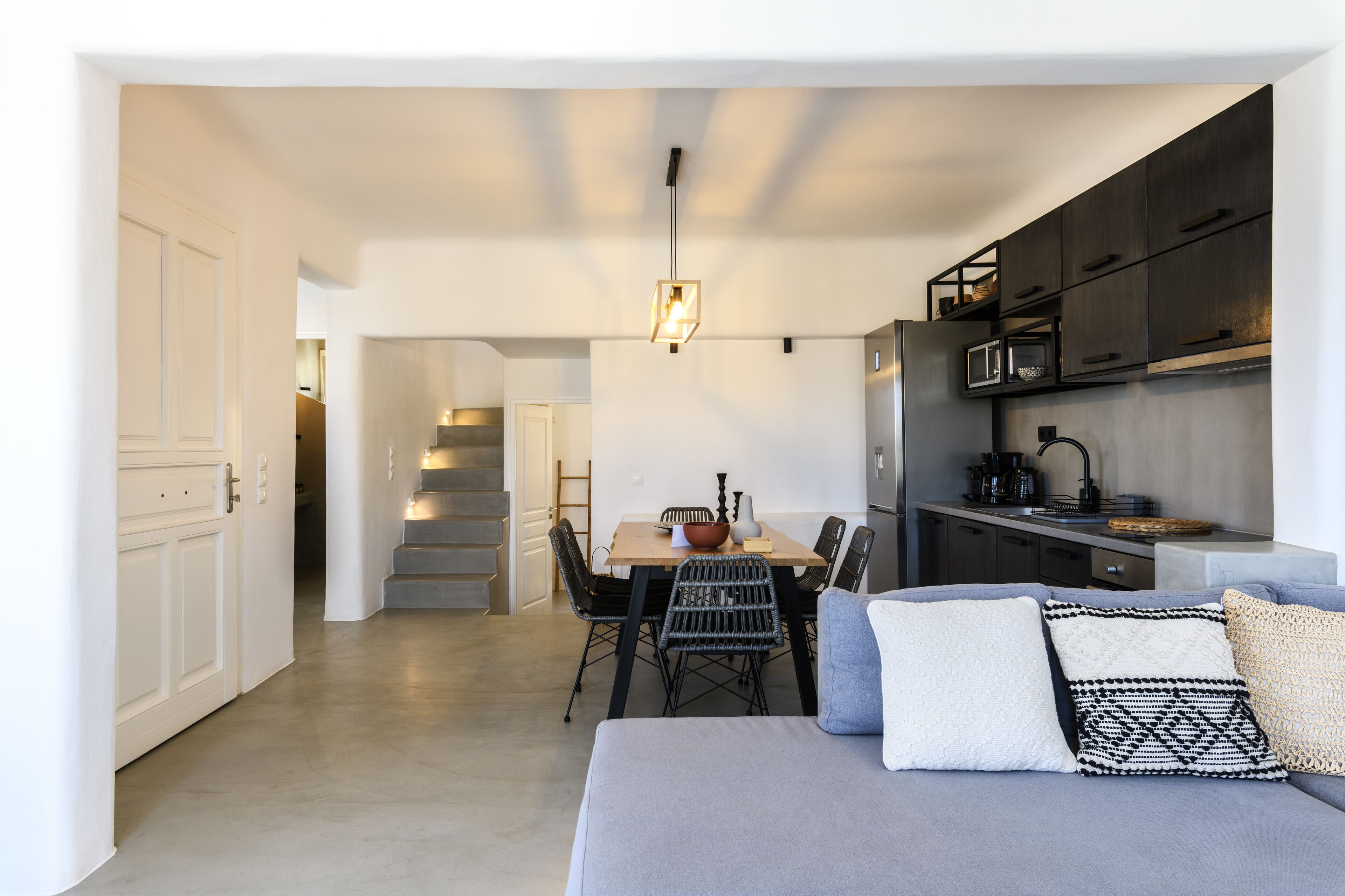 A modern kitchen with dark cabinets, a dining area with a wooden table and chairs, and a staircase leading to another level.