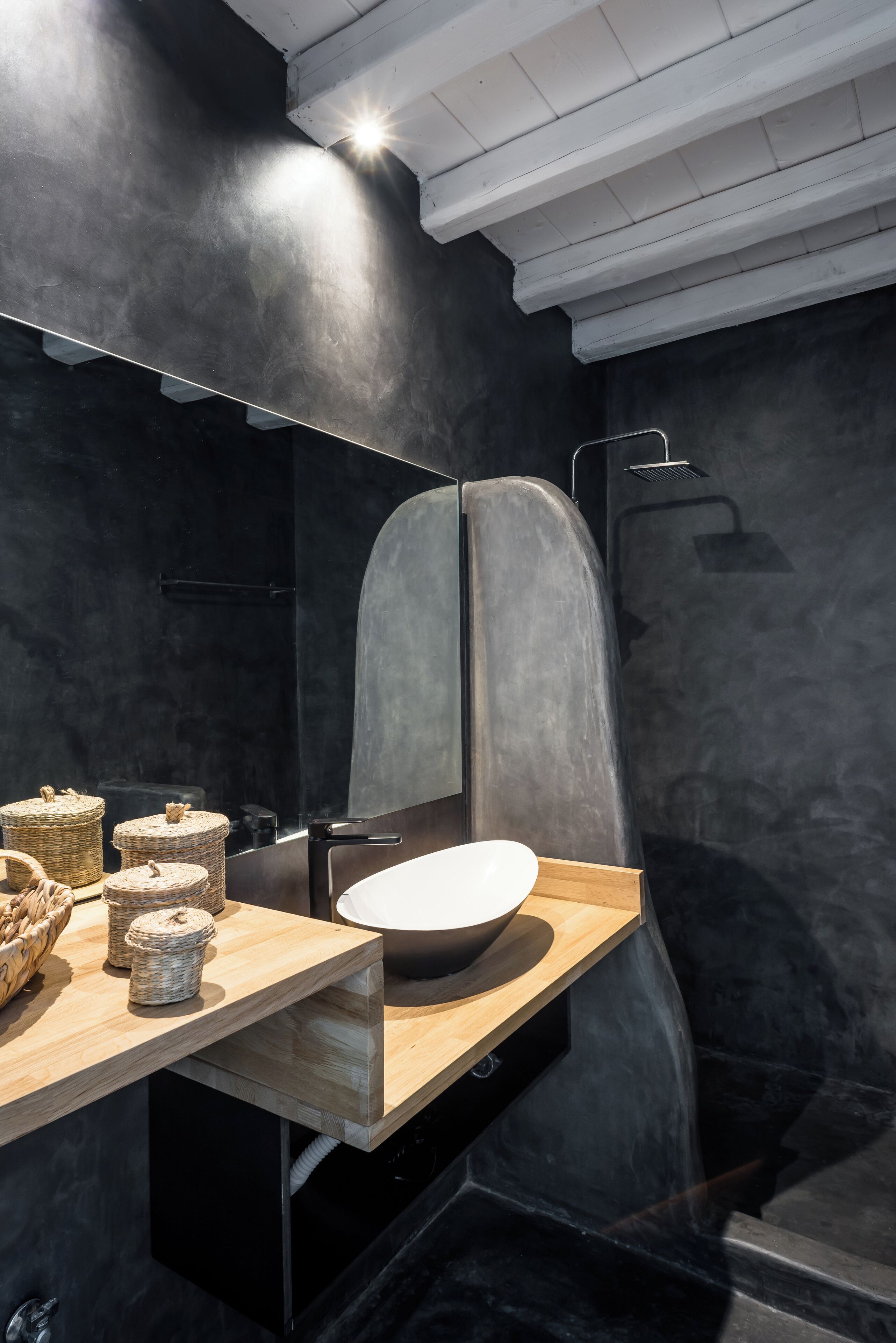 A modern bathroom with a dark, textured wall, a wooden vanity, a large mirror, and a shower area.