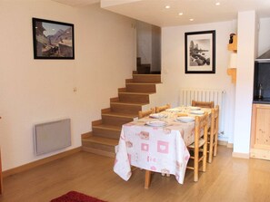 A dining area with a table set for four, wooden chairs, a staircase, and framed pictures on the walls. - Cozy Duplex Ski Apartment, 4-5 Beds, Vars Les Claux, Close to Pistes and Shops (Vars)