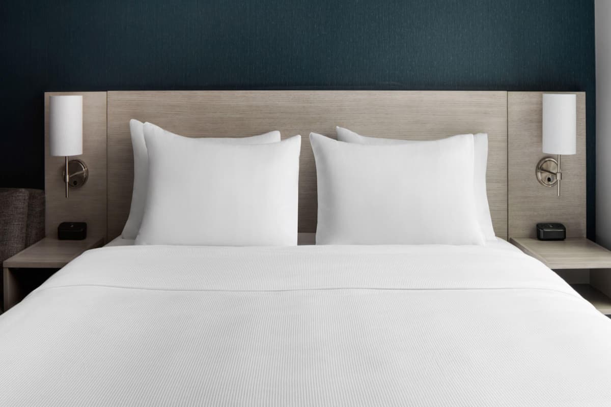 A hotel room with a bed, two nightstands, and wall-mounted lamps.