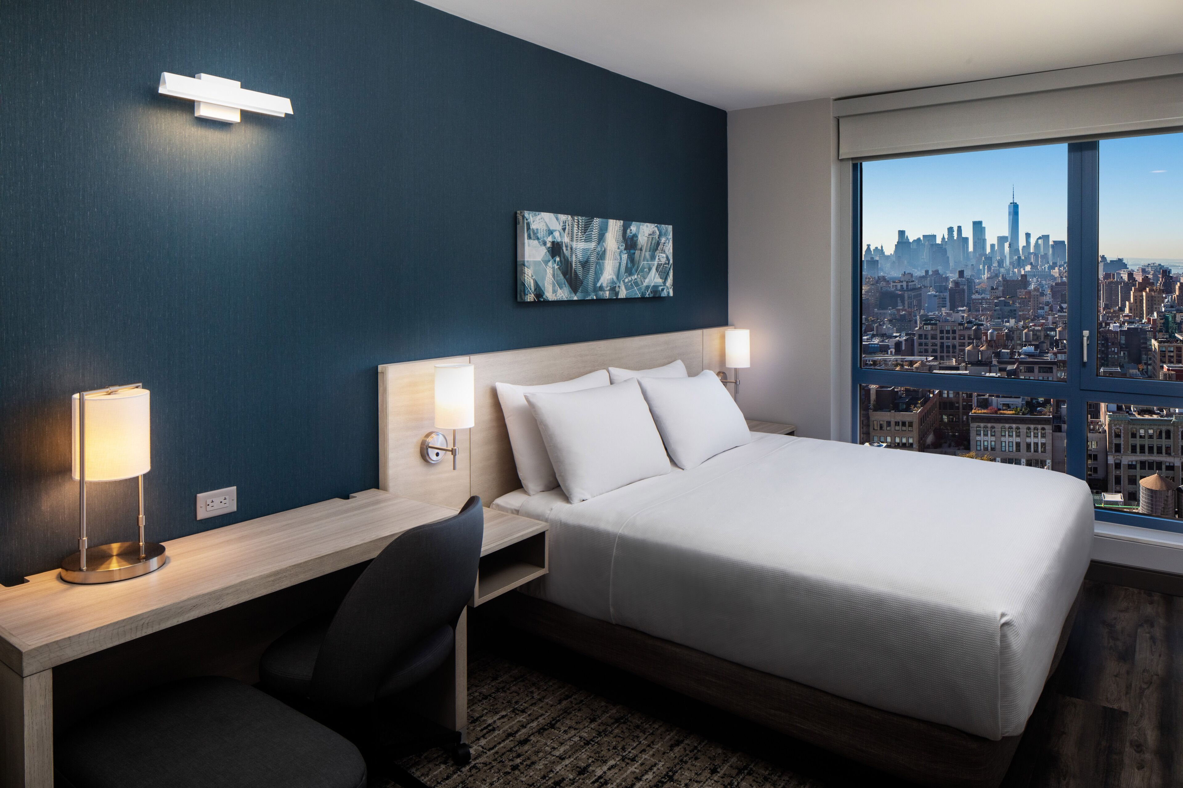 Ein Hotelzimmer mit Bett, Schreibtisch, Stuhl und Blick auf die Stadt.