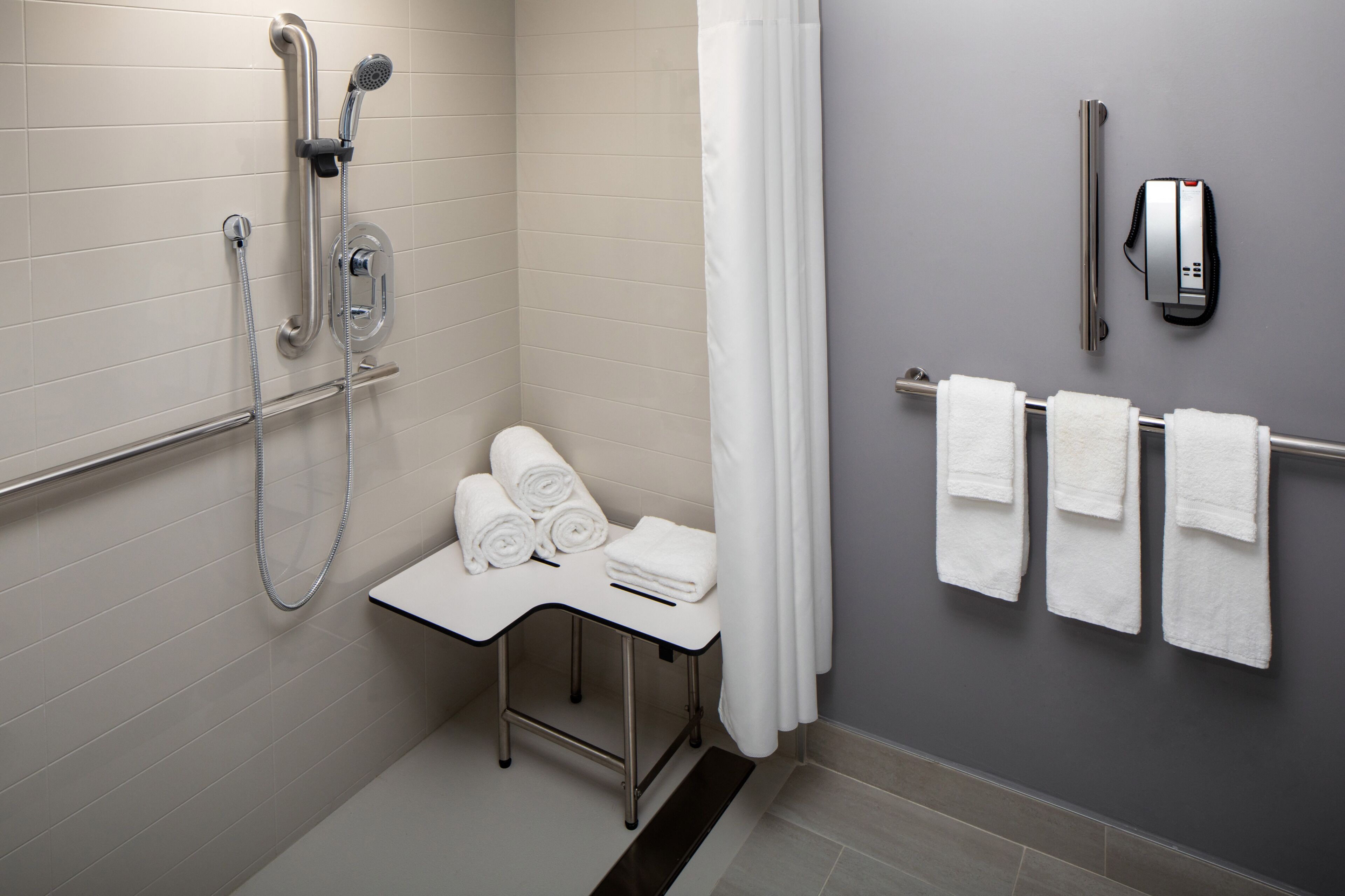 Un baño con ducha, un perchero y una mesita con toallas.