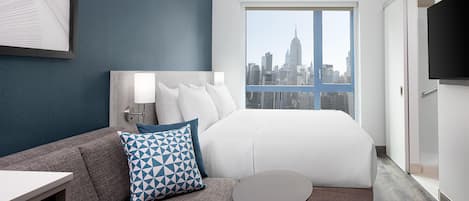 A hotel room with a bed, a sofa, a small table, a TV, and a city view.