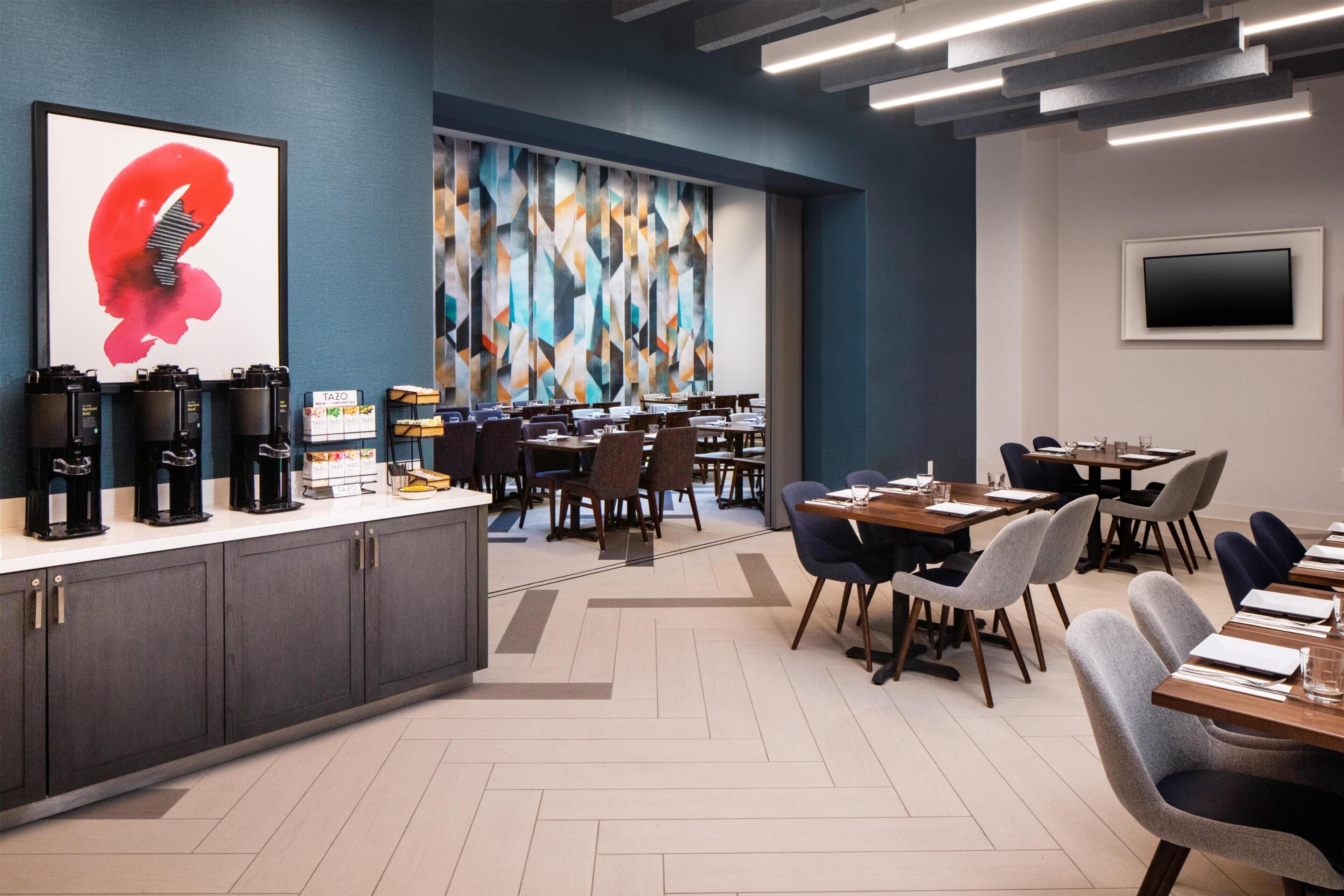A modern conference room with a large abstract painting, a coffee station, and a TV mounted on the wall.