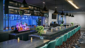 A bar area with a long counter, bar stools, pendant lighting, and a view of the outside. - Hyatt Place New York / Chelsea (New York)