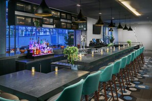 A bar area with a long counter, bar stools, pendant lighting, and a view of the outside.