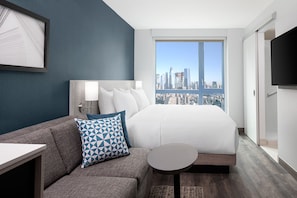 A hotel room with a bed, a sofa, a small table, a TV, and a city view.