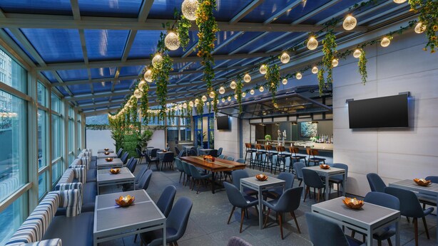 A restaurant with a glass ceiling, tables with blue chairs, and hanging plants. - Hyatt Place New York / Chelsea (New York)