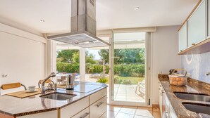 Une cuisine moderne dotée d’un grand îlot central, de deux éviers et d’une porte-fenêtre coulissante donnant sur un patio.