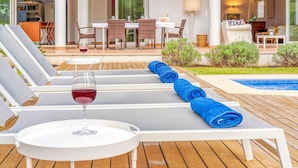 Un espace aménagé au bord de la piscine, avec des chaises longues, une table sur laquelle est posé un verre de vin rouge et une petite piscine.
