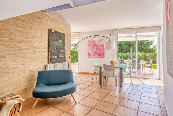 Una sala de estar moderna con un sofá azul, un comedor con mesa de vidrio y vistas a un jardín a través de amplios ventanales corredizos.