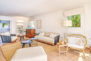 Un salon comprenant un canapé, deux fauteuils, une table basse, une lampe, un radiateur et une fenêtre avec des rideaux.