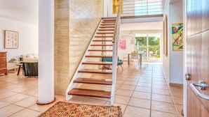 Un intérieur spacieux avec un escalier en bois, une grande colonne et une vue sur un espace extérieur.