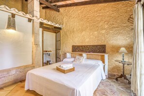 Une chambre à coucher avec un lit, une tête de lit en bois, une petite table avec une lampe et un mur en pierre.