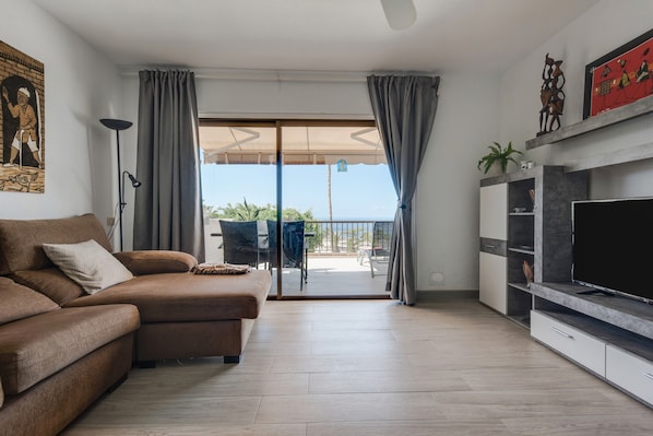 A living room with a sofa, TV, and a balcony with a view.