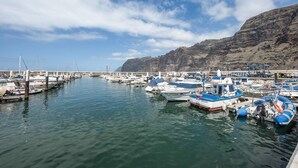 Uma marina com barcos atracados, uma ponte ao fundo e uma paisagem montanhosa.