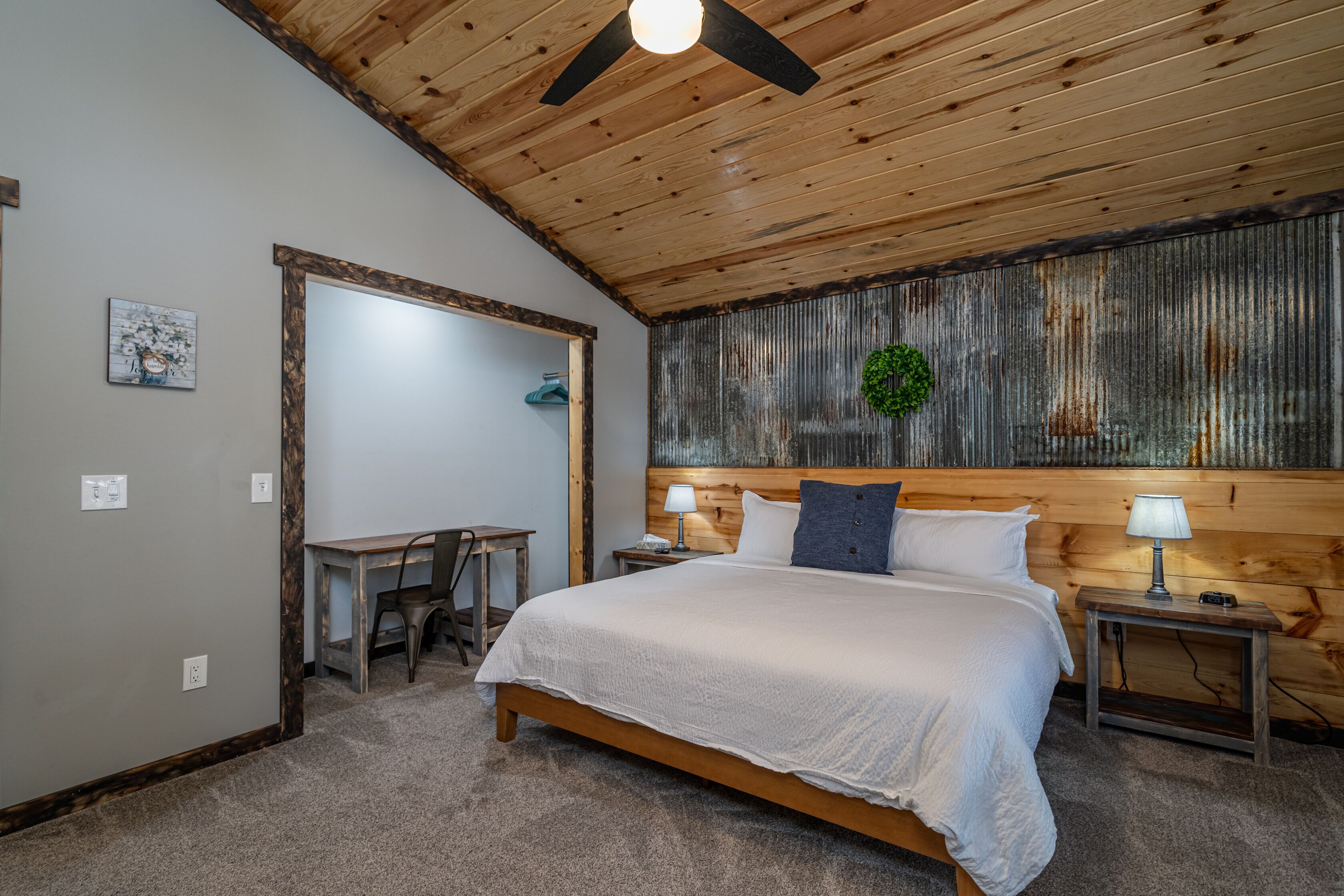 Une chambre avec un plafond en bois, un lit avec une literie blanche, deux tables de chevet avec des lampes, un petit bureau et une chaise.