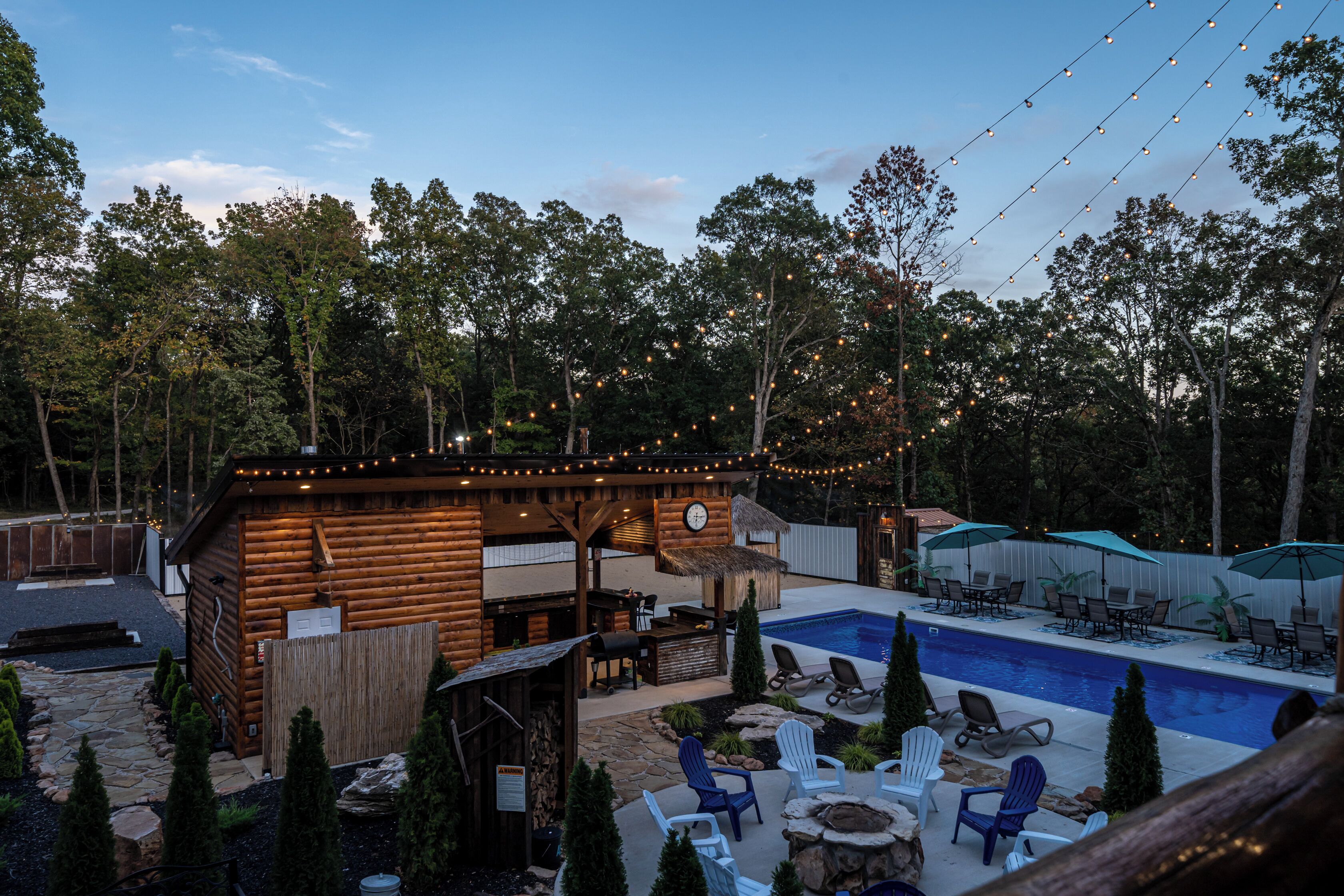 Une cabane en bois avec une piscine, entourée d’arbres et dotée d’un espace salon extérieur.