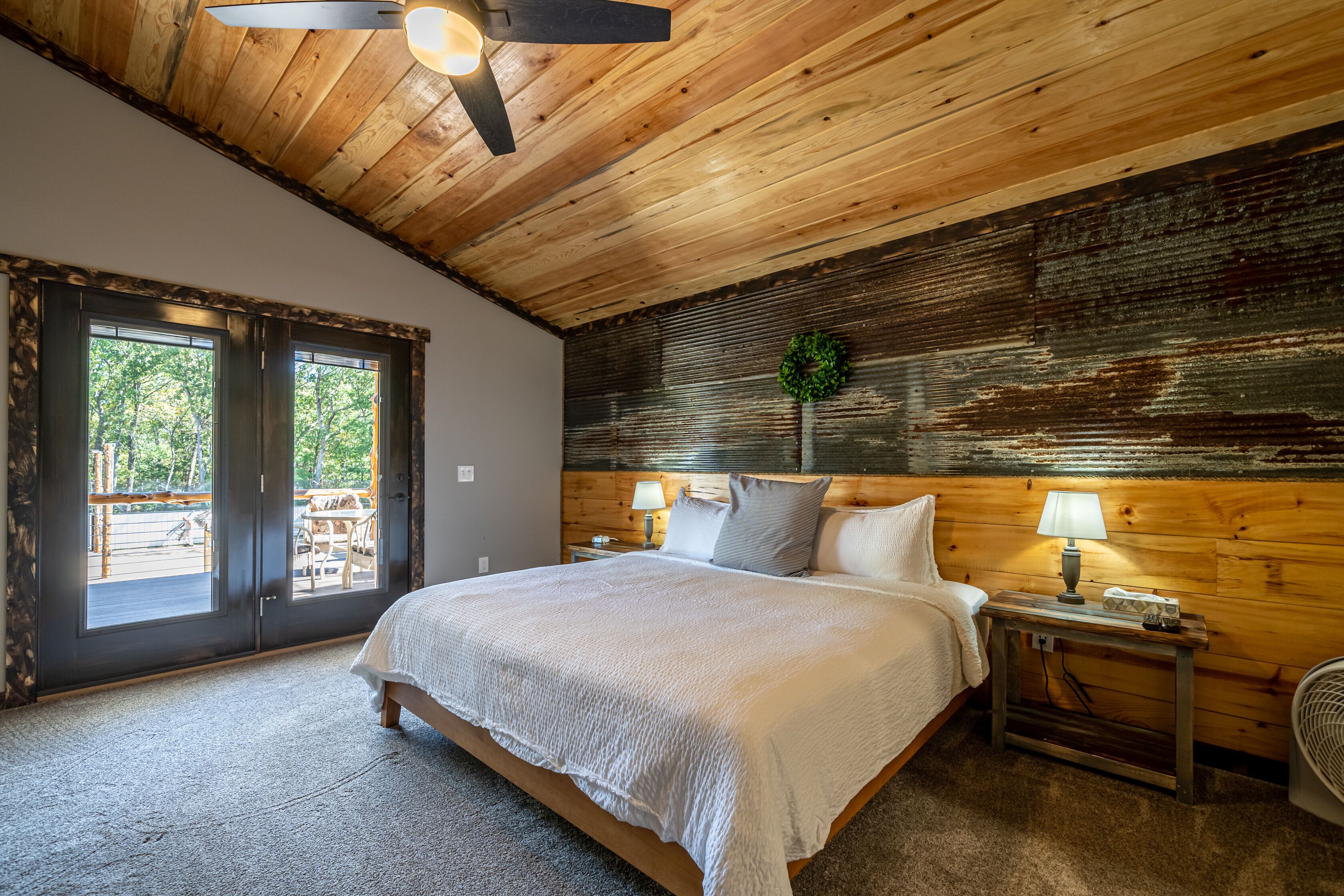 A bedroom with a large bed, wooden ceiling, and a view through the glass doors.