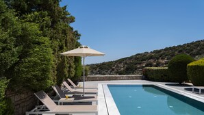 Uma área de piscina com espreguiçadeiras e um guarda-sol, cercada por vegetação e vista para uma paisagem montanhosa.