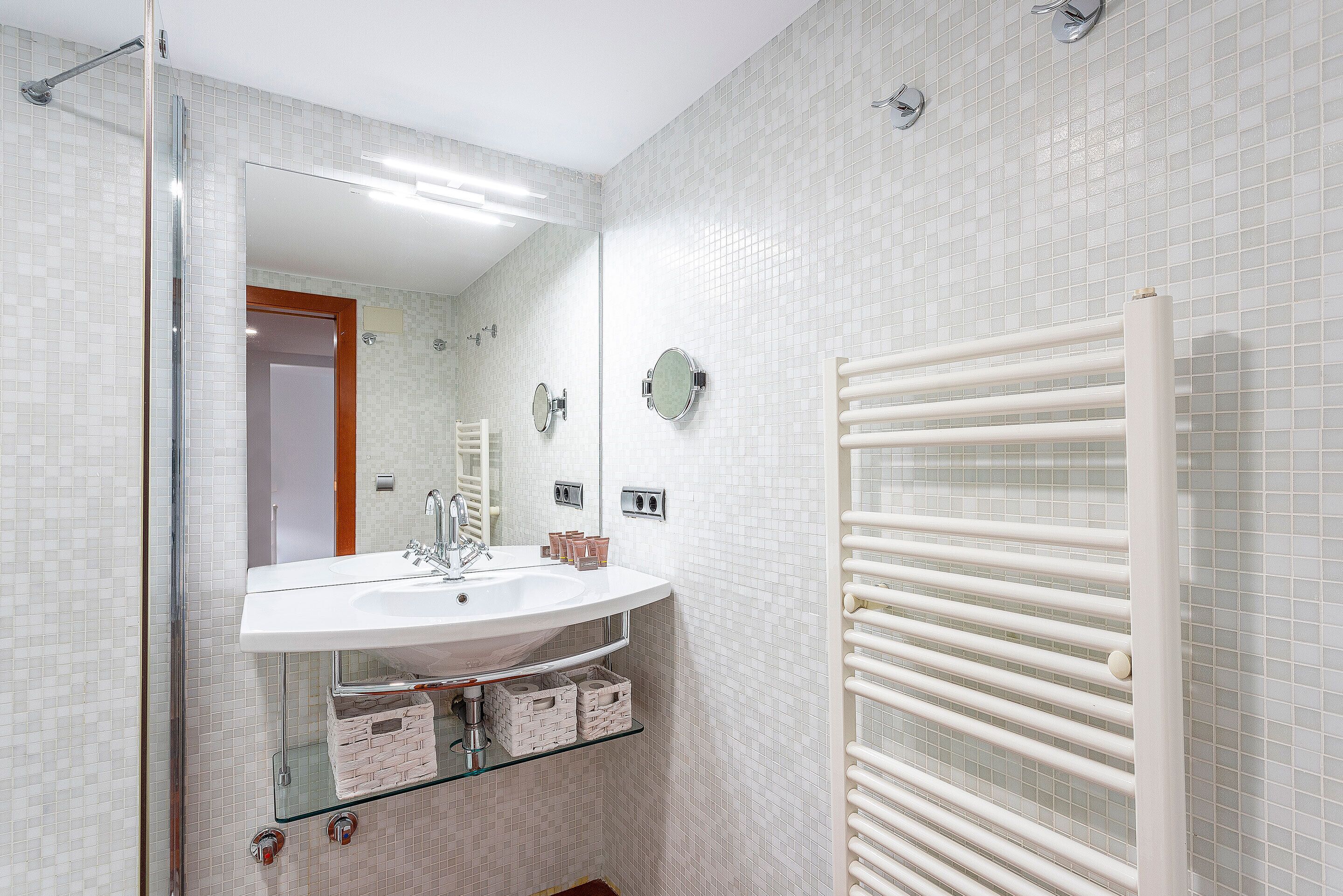 A bathroom with a white sink, glass shelves, a mirror, and a towel rack.
