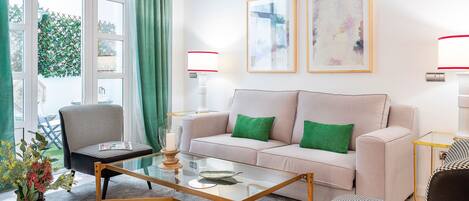 Ein Wohnzimmer mit einer Couch, Sesseln, einem Glastisch und einer Blumenvase.