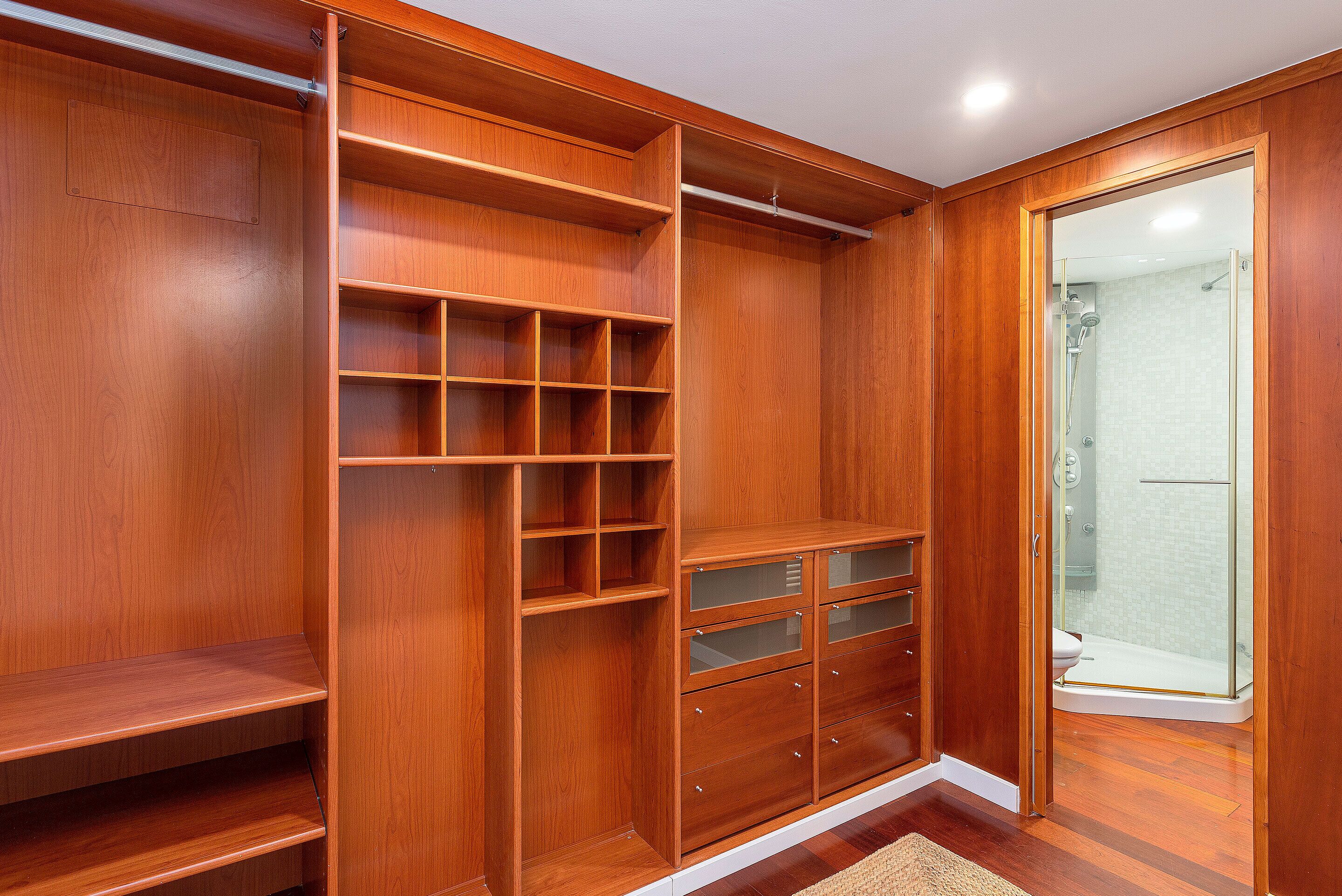 A wooden closet with multiple shelves and drawers, a glass shower door, and a wooden floor.