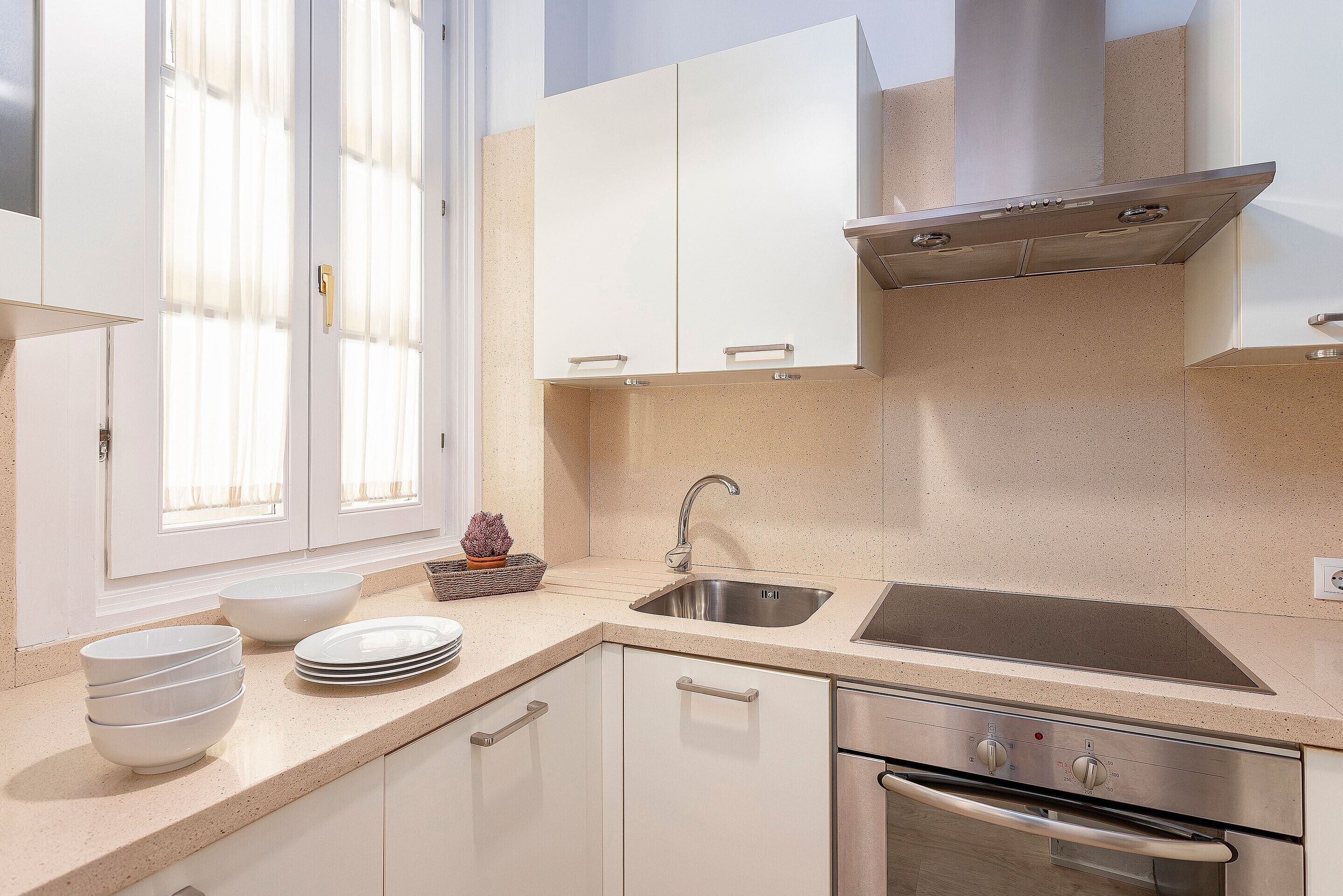 A modern kitchen with white cabinets, a stainless steel sink, and a built-in oven.