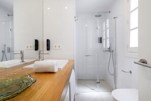 Un baño moderno con cabina de ducha de vidrio, tocador de madera con lavabo de cristal y un inodoro blanco.