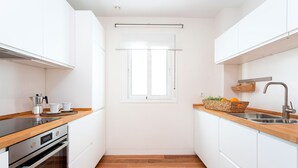 Eine moderne Küche mit weißen Schränken, einer Holz Arbeitsplatte, einem Einbauofen, einem Fenster und einer Spüle mit Obstkorb.