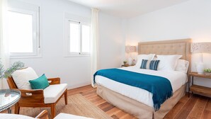 Ein Schlafzimmer mit Bett, Sessel, Nachttisch und einer Lampe.