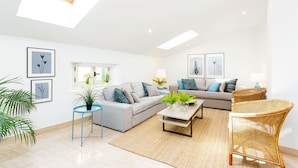 A modern living room with a sofa, coffee table, and wicker chairs. There are potted plants and framed artwork on the walls. - Genteel Home Marin Garcia IV (Málaga)