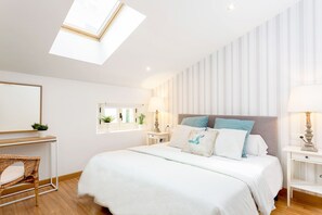 A bedroom with a skylight, a bed with white bedding, a bedside table with a lamp, and a chair.