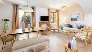 Een helder verlicht zithoek met een eettafel, stoelen, een bank en een televisie.