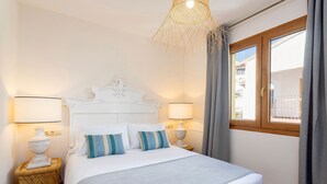 Een net opgemaakt bed met een wit hoofdeinde, twee bedlampen en een raam met gordijnen.
