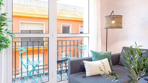 A balcony with a blue chair and a table, a grey sofa with cushions, and a floor lamp. - 1 Bd Apartment With Balcony Perfect Location. Santa Marta II (Seville)