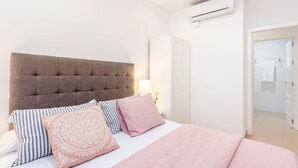 A bedroom with a tufted headboard, a bed with pink and striped bedding, and a white wardrobe. - Genteel Home Marin Garcia I (Málaga)
