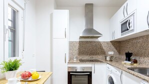A compact kitchen with white cabinets, a granite countertop, a stainless steel range hood, a built-in oven, a washing machine, and a microwave. - Genteel Home Marin Garcia I (Málaga)