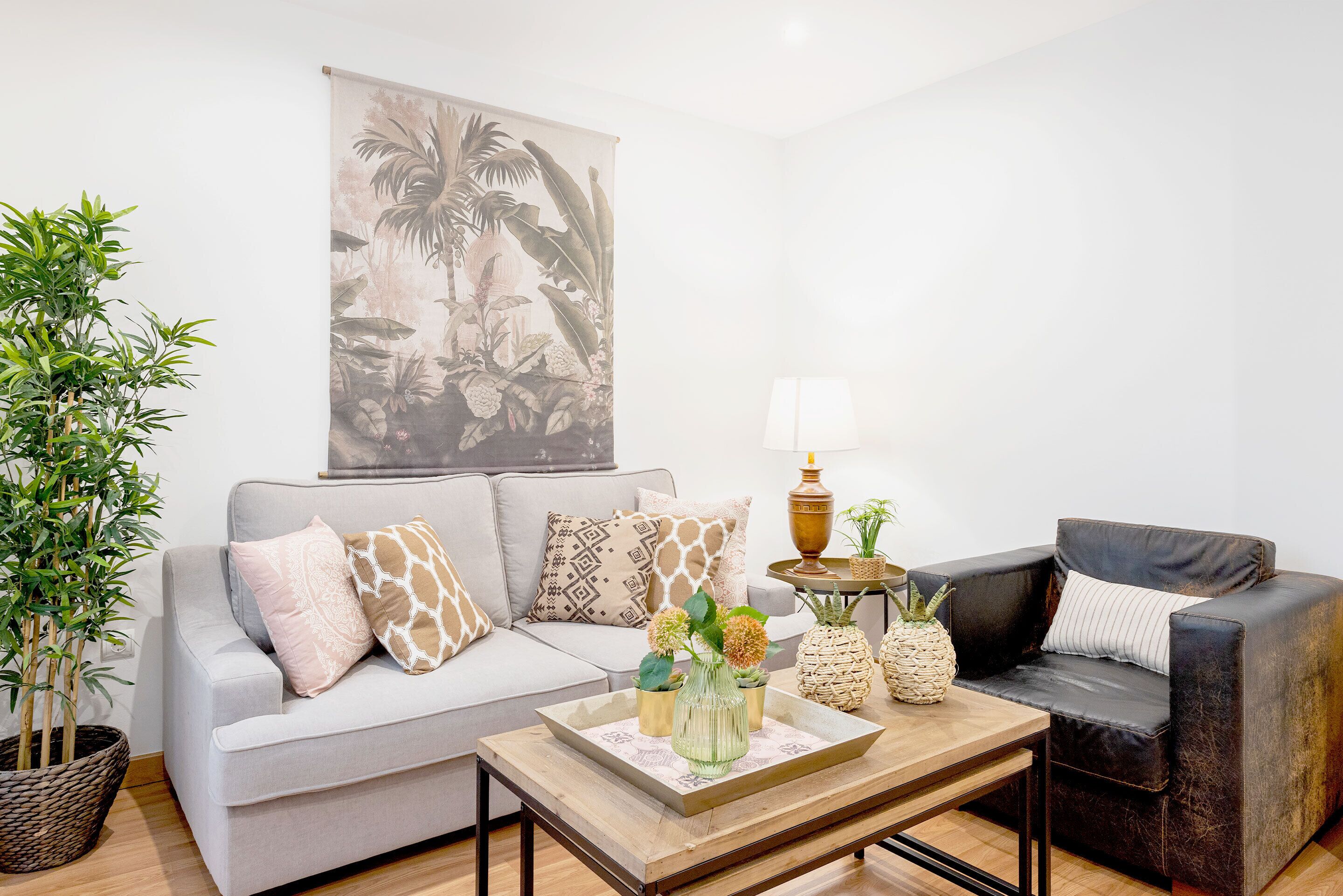 Ein Wohnzimmer mit grauem Sofa, einem schwarzen Sessel, einem Couchtisch, einer Lampe und einem großen Wandteppich.