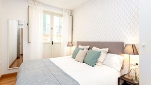A bedroom with a large bed, a nightstand with a lamp, and a window with curtains.