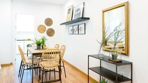 A dining area with wicker chairs, a wooden table, and a black console table with a mirror and plants.