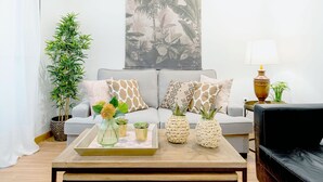 A living room with a sofa, a coffee table with decorative items, a potted plant, and a wall tapestry.