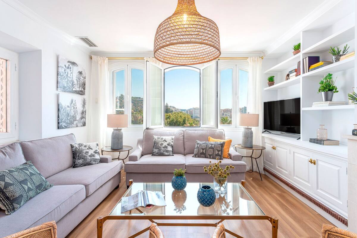 A modern living room with a sofa, coffee table, and large windows offering a city view.