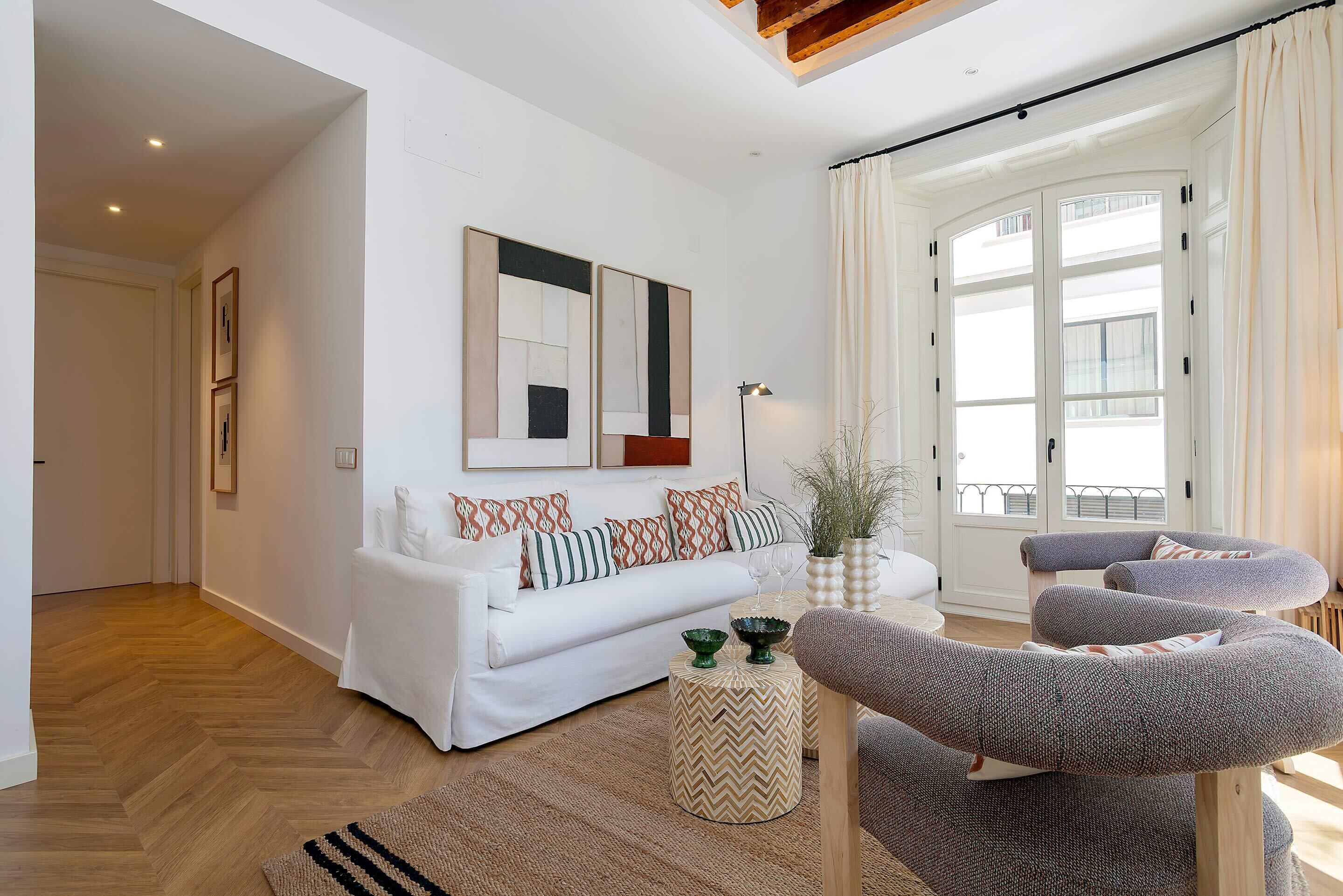 A modern living room with a white sofa, patterned cushions, a round coffee table, and a gray armchair.